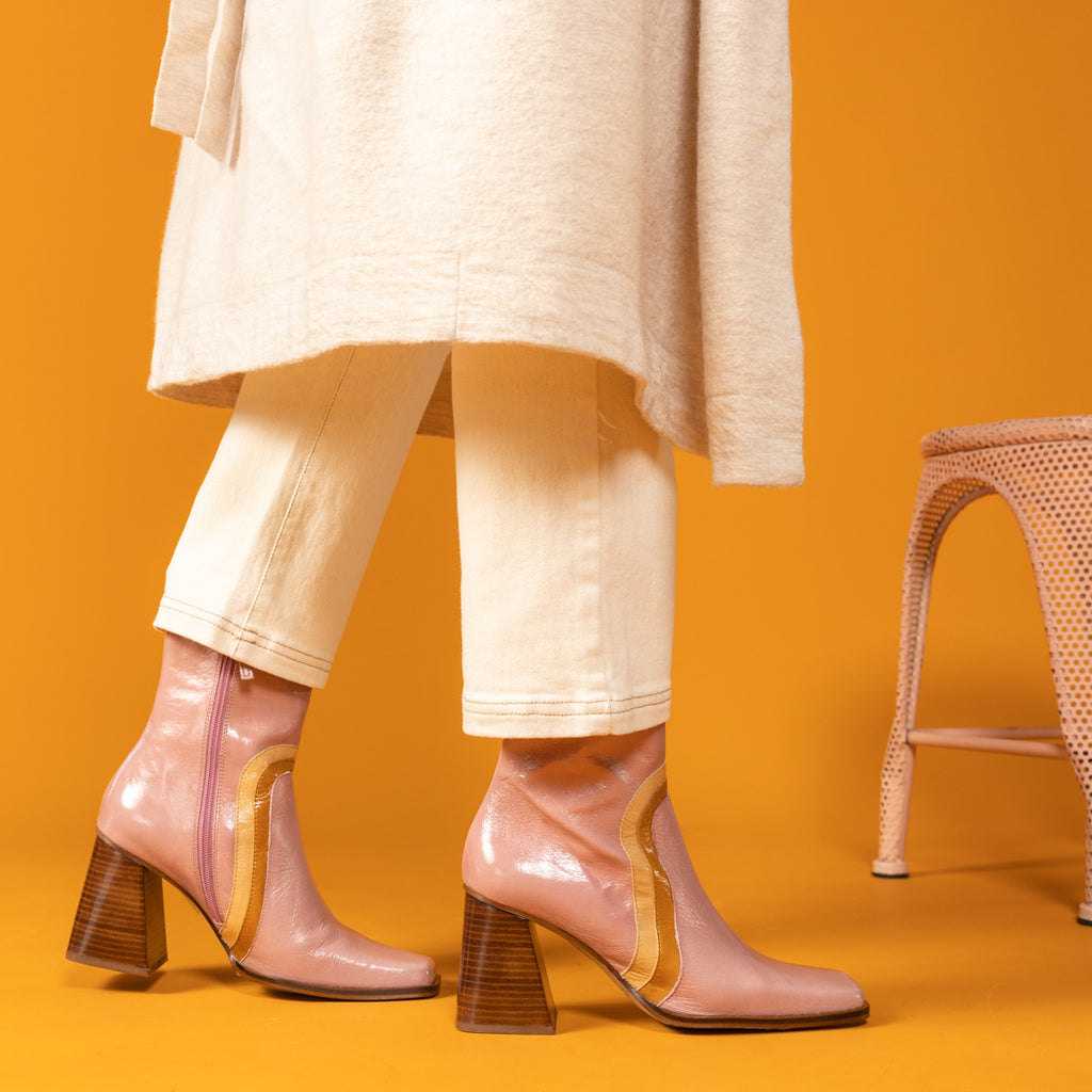 Woman in Cream Jeans and Jacket wearing pink 70's style boots with a tan and caramel stripe and wood block heel on an orange background