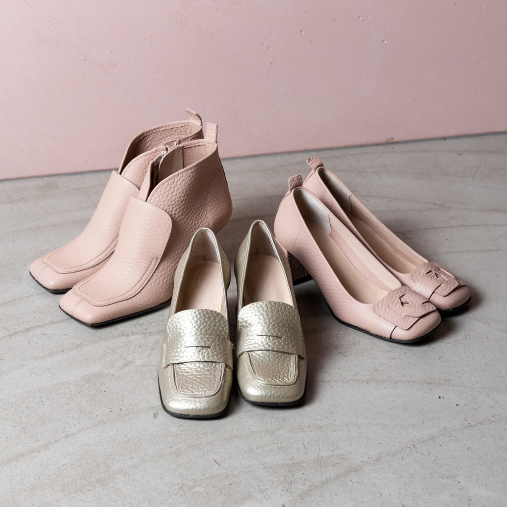 Collection of pink and gold shoes on concrete floor with pink background