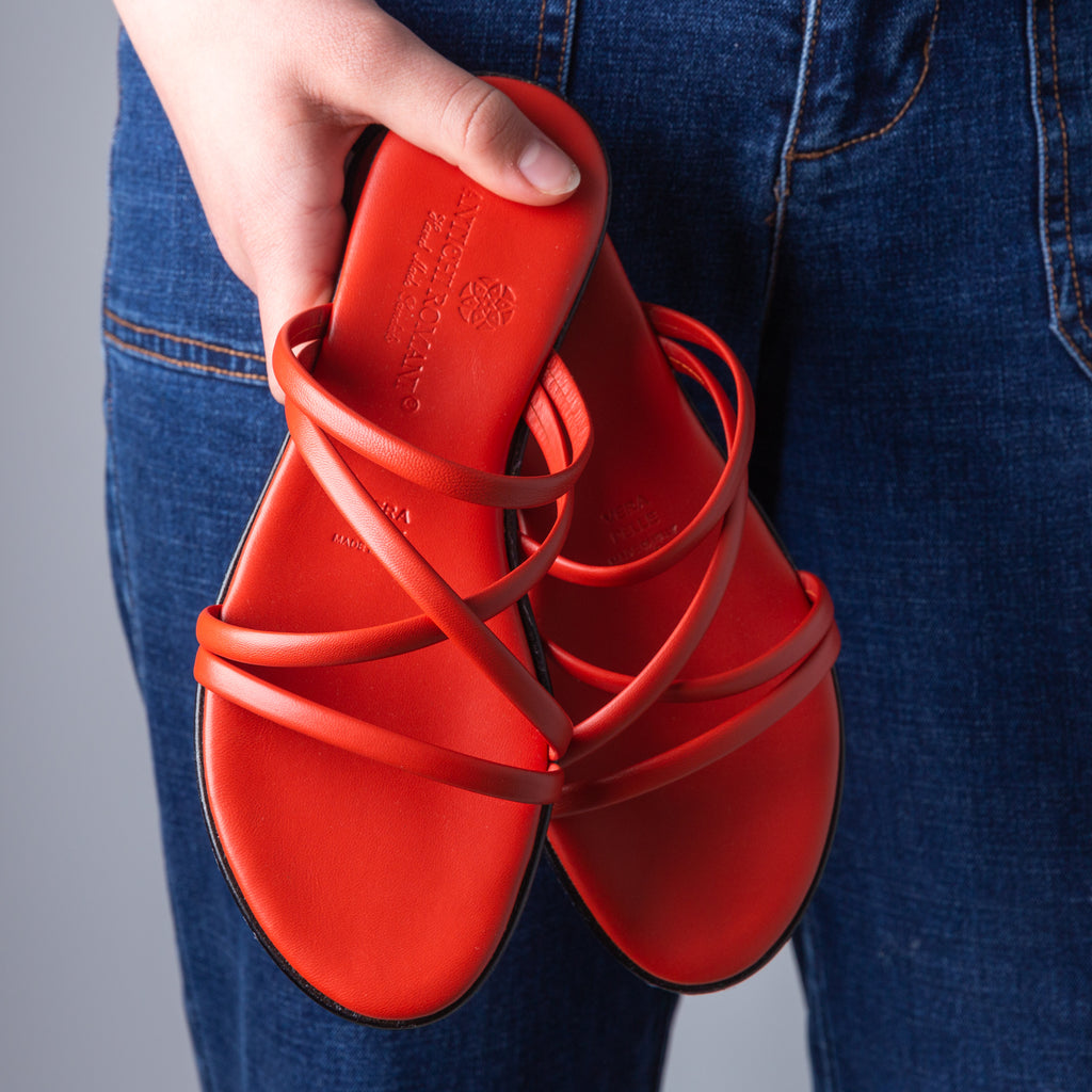 Woman holding red strappy leather sandals against denim jeans