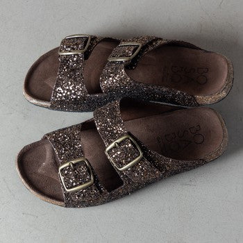 bronze Glitter covered two strap sandals look like birkenstocks on a grey concrete floor