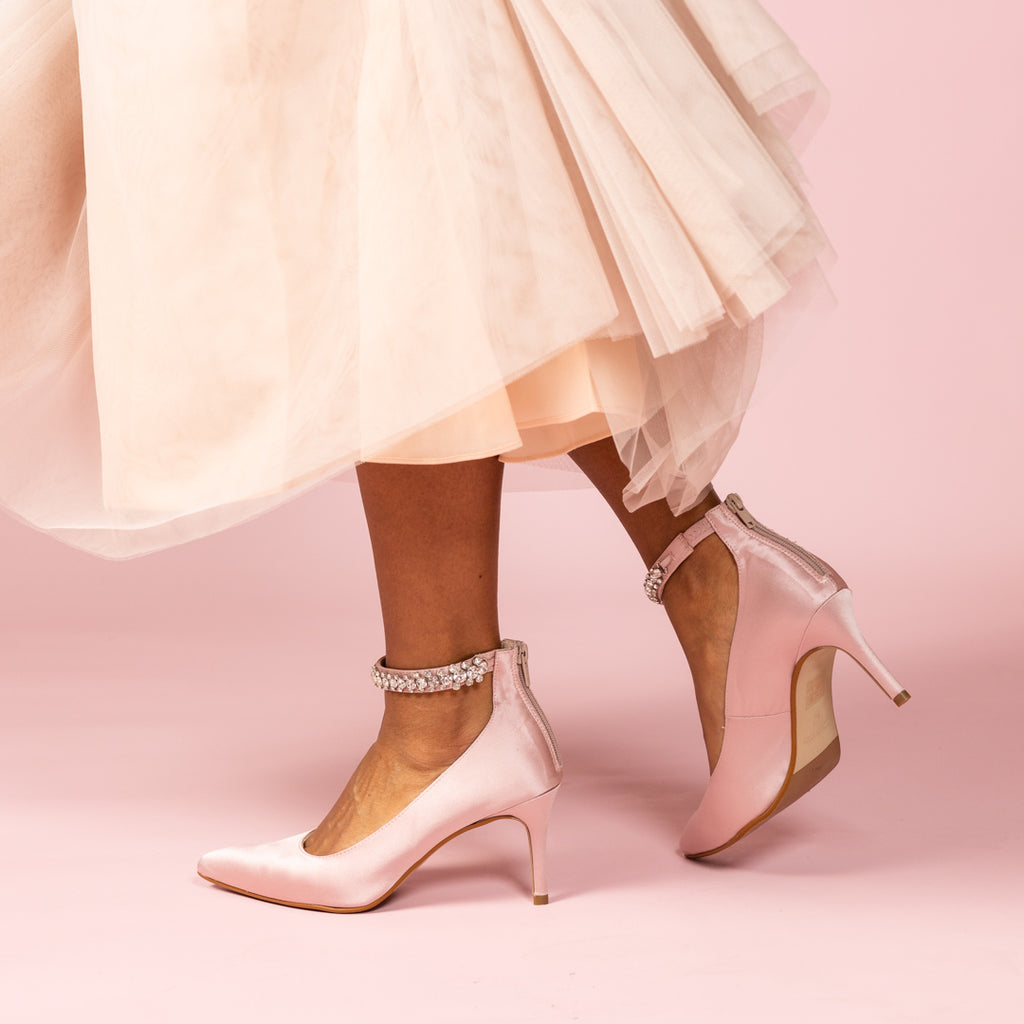 Lady wearing pale pink satin heels with a diamante ankle strap and tulle skirt on pale pink background